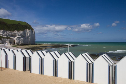Beach huts and coastal cliffs at Flower Camping La Chênaie, a holiday park in scenic Normandy, France.