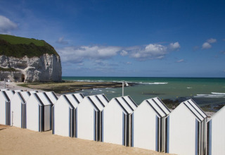 Beach huts and coastal cliffs at Flower Camping La Chênaie, a holiday park in scenic Normandy, France.