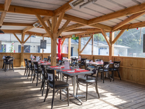 Covered outdoor dining area with wooden beams and cow-print chairs at Flower Camping La Chênaie in Normandy, France.