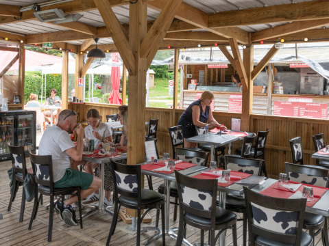 Outdoor dining area at Flower Camping La Chênaie in Normandy, France, with guests and a waitress serving.