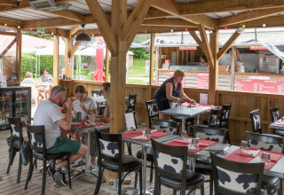 Udendørs restaurantområde på Flower Camping La Chênaie i Normandiet, Frankrig, med gæster og personale.