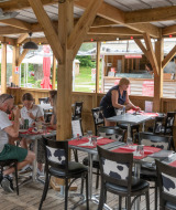 Buiten eetgedeelte bij Flower Camping La Chênaie in Normandië, Frankrijk, met gasten en serveerster.