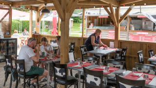Outdoor dining area at Flower Camping La Chênaie in Normandy, France, with guests and a waitress serving.