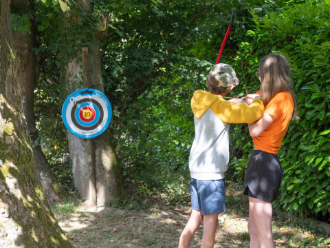 Dos niños practican tiro con arco junto a una diana en Flower Camping La Chênaie en Normandía, Francia.