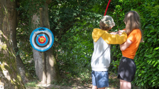 Two children practicing archery by a target at Flower Camping La Chênaie holiday park in Normandy, France.