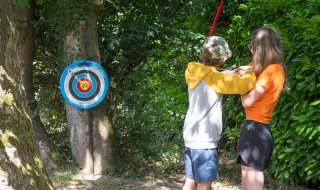 Twee kinderen doen aan boogschieten bij een doel op Flower Camping La Chênaie in Normandië, Frankrijk.