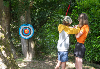 Zwei Kinder üben Bogenschießen im Wald beim Flower Camping La Chênaie in der Normandie, Frankreich.