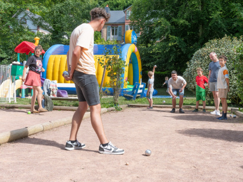 Børn og voksne leger petanque ved siden af en oppustelig forlystelse i Flower Camping La Chênaie i Normandiet.