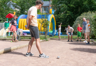 Børn og voksne leger petanque ved siden af en oppustelig forlystelse i Flower Camping La Chênaie i Normandiet.