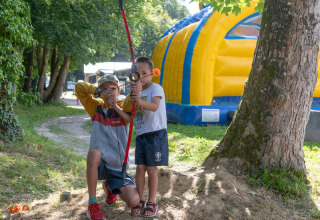 Deux enfants jouent à l’arc dans un parc près d’une grande structure gonflable jaune et bleue.