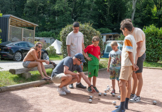 Familie spiller petanque udendørs på Flower Camping La Chênaie i Normandiet, Frankrig, omgivet af natur.