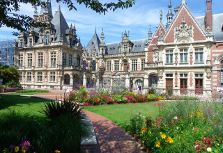 Wunderschönes historisches Schloss mit Türmen und Blumenbeeten im Flower Camping La Chênaie, Normandie.