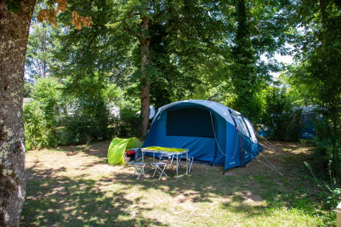 Campingplatz mit Zelt, Tisch und Stühlen unter Bäumen im Flower Camping La Sagne, Nouvelle-Aquitaine, Frankreich.