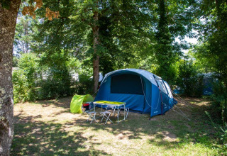 Campingplatz mit Zelt, Tisch und Stühlen unter Bäumen im Flower Camping La Sagne, Nouvelle-Aquitaine, Frankreich.