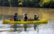 Tres personas y un perro reman en una canoa amarilla en un río en Flower Camping La Sagne, Francia.