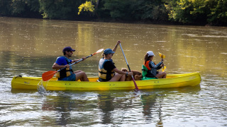 Tre persone e un cane remano in una canoa gialla sul fiume a Flower Camping La Sagne, in Francia.