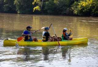 Drei Personen und ein Hund paddeln in einem gelben Kanu auf einem Fluss bei Flower Camping La Sagne.