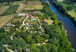 Luftfoto af Flower Camping La Sagne feriepark i Nouvelle-Aquitaine, Frankrig, omgivet af grønne marker og en flod.