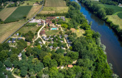 Luftfoto af Flower Camping La Sagne feriepark i Nouvelle-Aquitaine, Frankrig, omgivet af grønne marker og en flod.