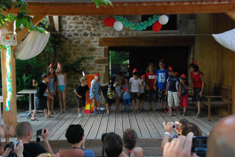 Kinder führen auf einer Holzterrasse bei einem Feriencamp im Flower Camping La Sagne in Frankreich auf.