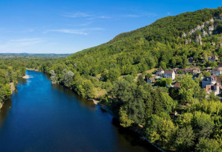 Aerial view of Flower Camping La Sagne holiday park with river, forested hills, and village in Nouvelle-Aquitaine, France.