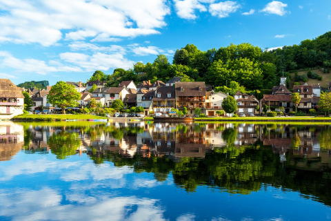 Vista panorámica de Vitrac en Nouvelle-Aquitaine, Francia, con pintorescas casas reflejadas en el río.