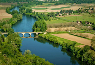 Vista aerea di campi verdi, un fiume tortuoso e un ponte presso Flower Camping La Sagne in Nouvelle-Aquitaine, Francia.