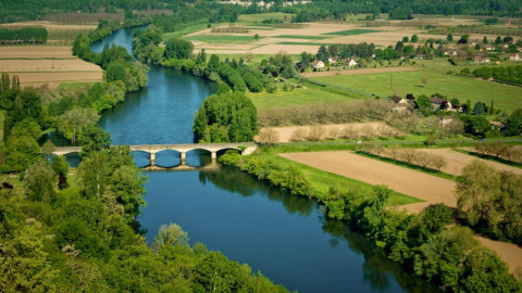Vista aérea de campos verdes, un río serpenteante y un puente en Flower Camping La Sagne en Nouvelle-Aquitaine, Francia.