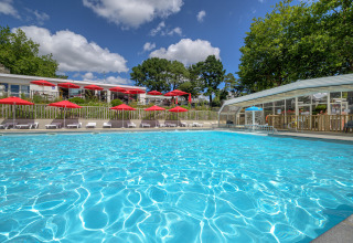 Udendørs swimmingpool med røde parasoller og liggestole på Flower Camping Le Conleau i Bretagne, Frankrig.