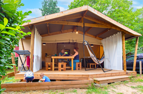 Gezin beleeft plezier voor een Ecolodge Cotton Confort safaritent op een camping tijdens de zomer.