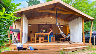 Familie nyder udendørslivet foran en Ecolodge Cotton Confort safari-telt på en campingplads om sommeren.