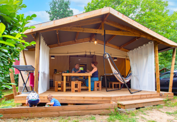 Familia disfruta de la vida al aire libre en el porche de una tienda safari Ecolodge Cotton Confort en camping.