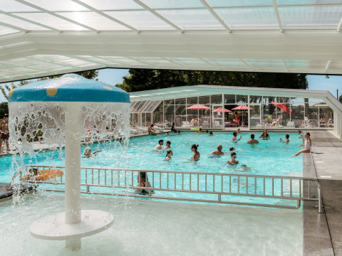 Piscina cubierta con fuente de agua y personas nadando en Flower Camping Le Conleau, Bretaña, Francia.