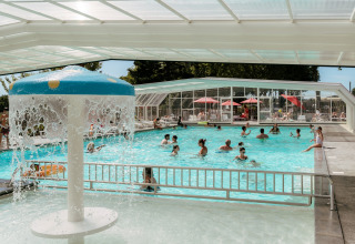 Indoor pool with water feature and people swimming, at Flower Camping Le Conleau holiday park in Brittany, France.