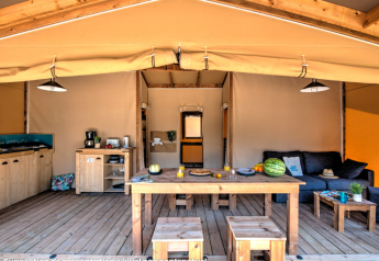Innenraum eines Safarizeltes mit Holzmöbeln, Küche, Sofa und Esstisch auf Holzboden.