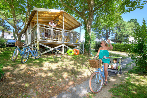 Family enjoying the outdoors at a cabin in Flower Camping Le Conleau holiday park, Brittany, France. Woman cycling.