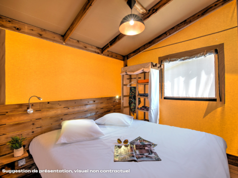 Acogedor dormitorio en tienda safari con cama doble, detalles de madera y luz natural abundante.
