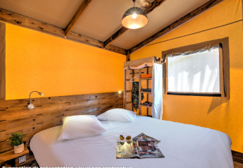 Gemütliches Schlafzimmer in einem Safarizelt mit Doppelbett, Holzelementen und Sonnenlicht.