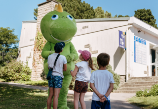 Niños saludan a una gran mascota verde al aire libre en un parque vacacional de Bretaña, Francia.