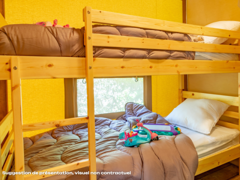 Interieur van een safaritent met houten stapelbedden, bruin beddengoed en speelgoed op het onderste bed.