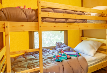 Interieur van een safaritent met houten stapelbedden, bruin beddengoed en speelgoed op het onderste bed.