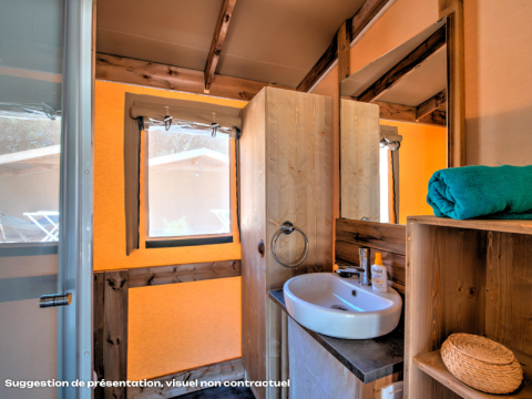 Interior de baño en tienda safari con lavabo, espejo, estantería, toalla enrollada y luz natural.