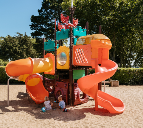 Niños juegan en la arena junto a un colorido parque infantil en Flower Camping Le Conleau, Bretaña, Francia.