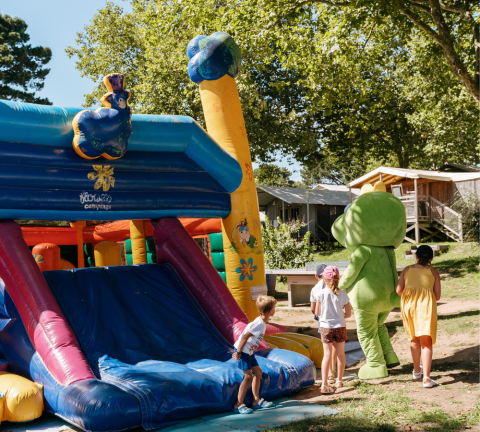 Kinderen spelen bij een opblaasglijbaan met een mascotte op een camping met huisjes in Bretagne, Frankrijk.