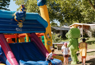 Kinderen spelen bij een springkasteel en mascotte op een camping met chalets in Bretagne, Frankrijk.