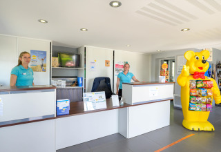 Receptie van Flower Camping Le Conleau in Bretagne, Frankrijk, met personeel en grote berenmascotte.