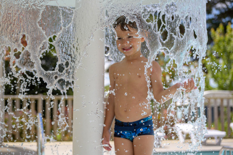 Child playing under cascading water in the pool at Flower Camping Le Conleau holiday park, Brittany, France.