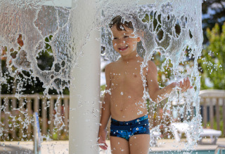 Niño juega bajo una cascada de agua en la piscina de Flower Camping Le Conleau, Bretaña, Francia.