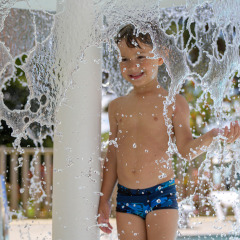 Barn leger under vandfald i swimmingpool i Flower Camping Le Conleau feriepark, Bretagne, Frankrig.