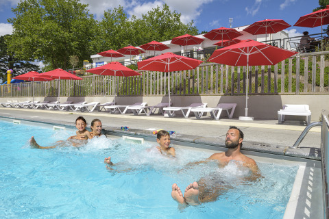 Familia divirtiéndose en la piscina con sombrillas rojas en Flower Camping Le Conleau, Bretaña, Francia.